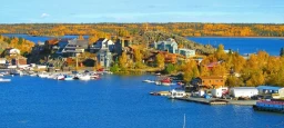 A beautiful landscape shot of Yellowknife's water front area. A number of houses, docks and boats can be seen along with autumn colored trees